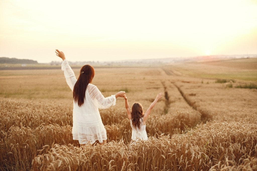 Mother and daughter holding hands with arms raised in a golden wheat field at sunset